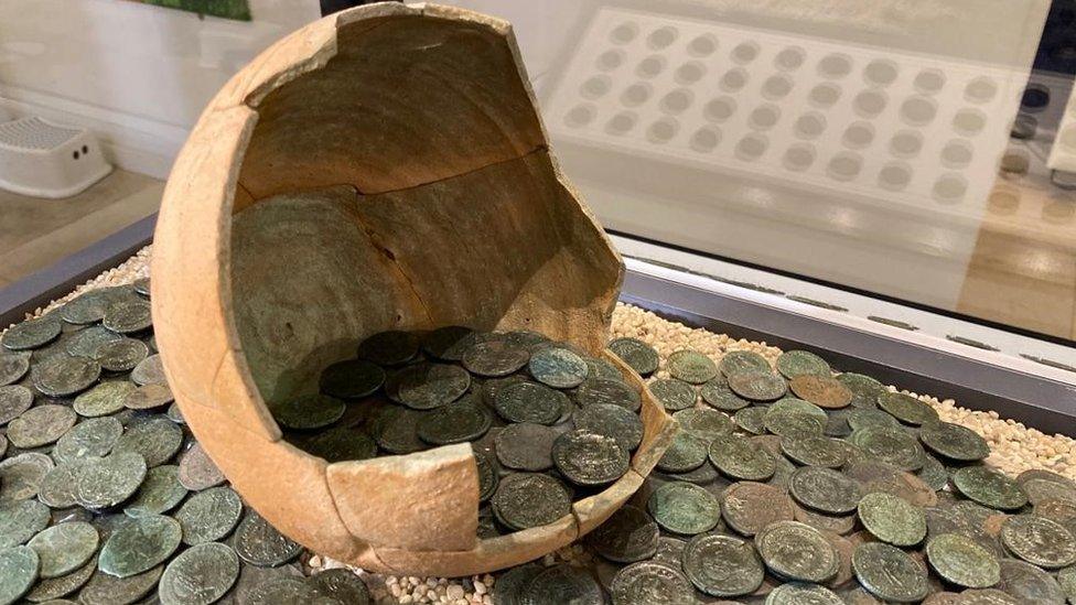 Broken pot holding coins with more coins scattered underneath