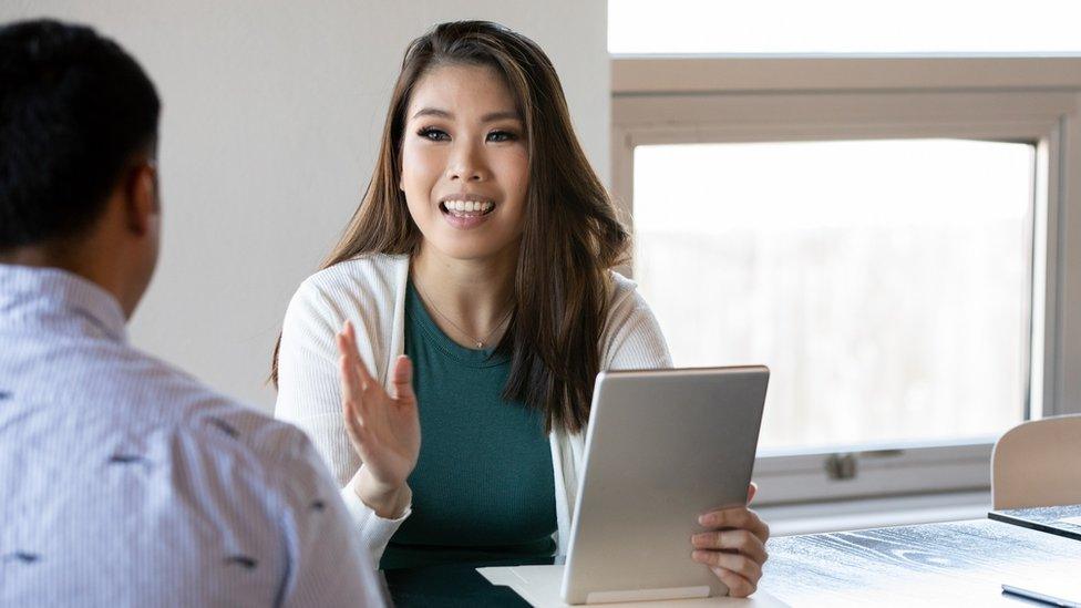 Woman holding tablet while talking to customer at desk