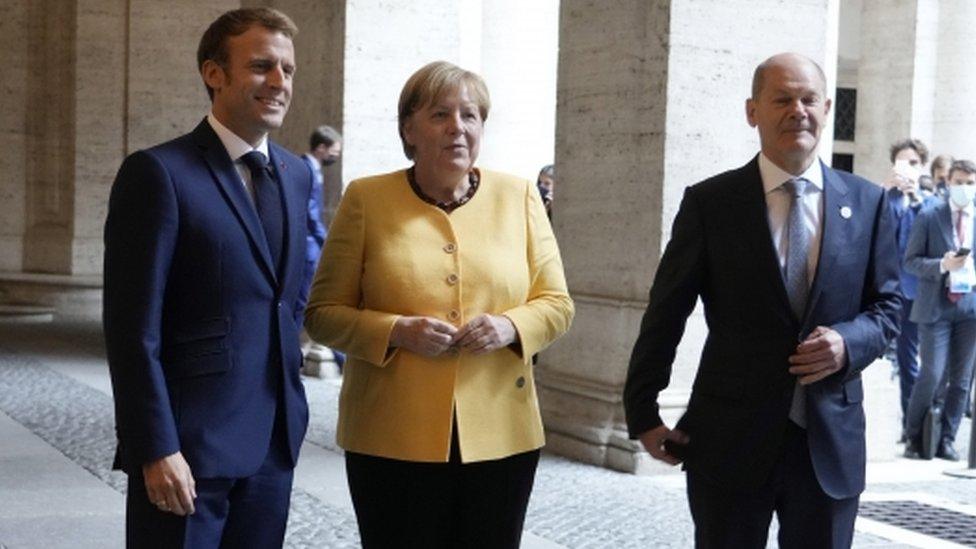 French President Emmanuel Macron, left, greets German Chancellor Angela Merkel, centre, and German Finance Minister Olaf Scholz, right, prior to a meeting of the European Union and the African Union at the French Embassy in Rome, Italy, 30 October 2021