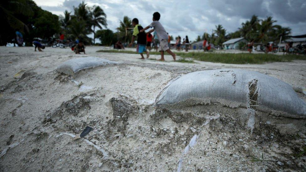 Kids play on an area of reclaimed land stacked with sandbags, a countermeasure to the rising in Funafuti, Tuvalu.