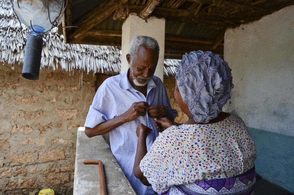 A woman buttons up her husband's shirt in Kenya