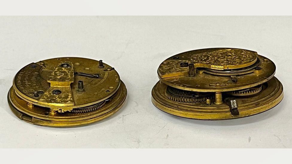 Side views of two mid-19th Century gold-coloured watch movements. The one on the right is slightly smaller than the one on the left. The views reveal each has two discs, one laid over the other with just glimpsed wheels in between.