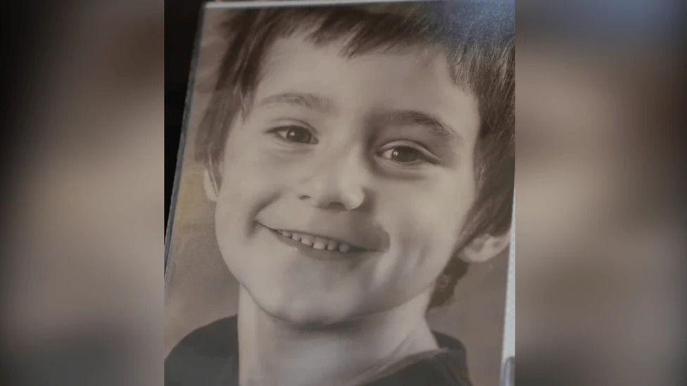 Daniel Klosi is seen smiling in a black-and-white portrait image. He is seen from the neck up.