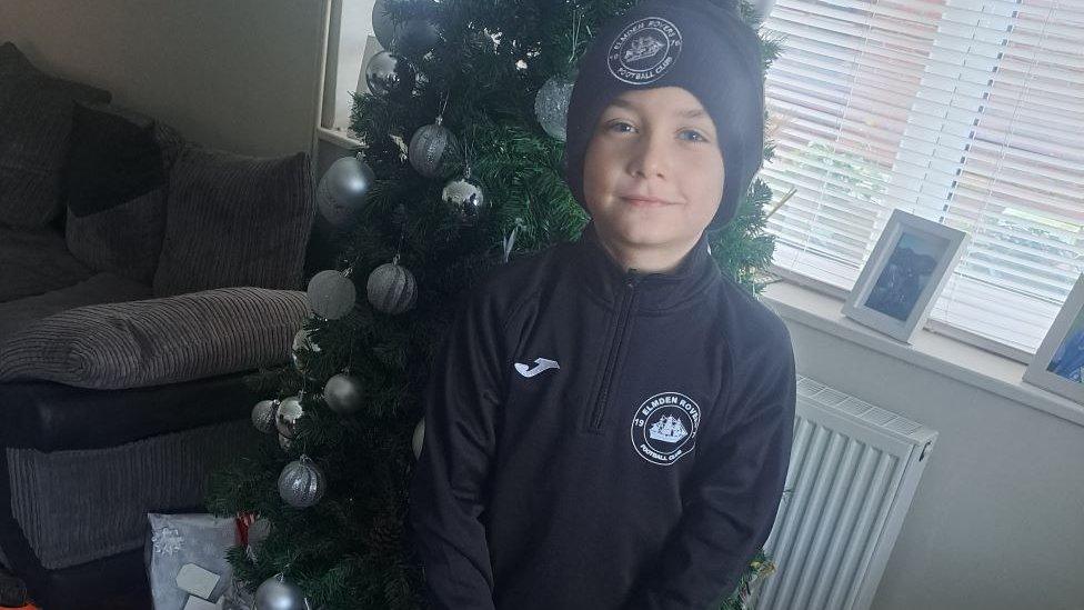 Harry in football kit, standing in front of a Christmas tree.