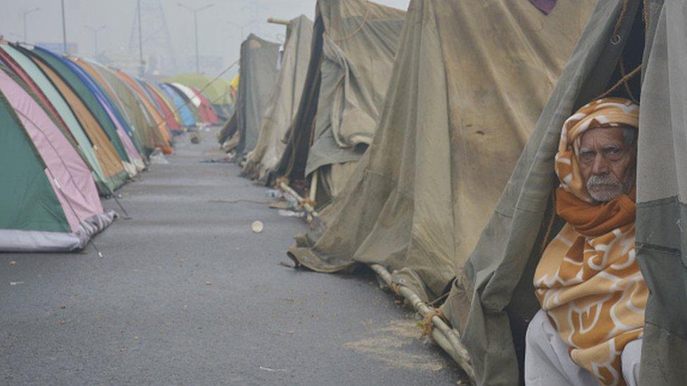 An elderly demonstrator looks on from a tent on a blocked section of a highway as farmers continue to camp in protest