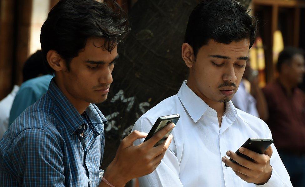 Indian pedestrians check their cellphones as they stand in front of the Bombay Stock Exchange (BSE) in Mumbai on September 29, 2016.