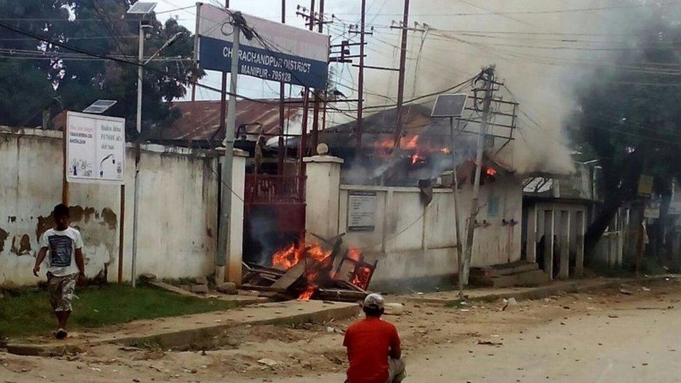 Indian pedestrians walk past a burning police station following violence in the Churachandpur district of the state of Manipur on September 1, 2015.