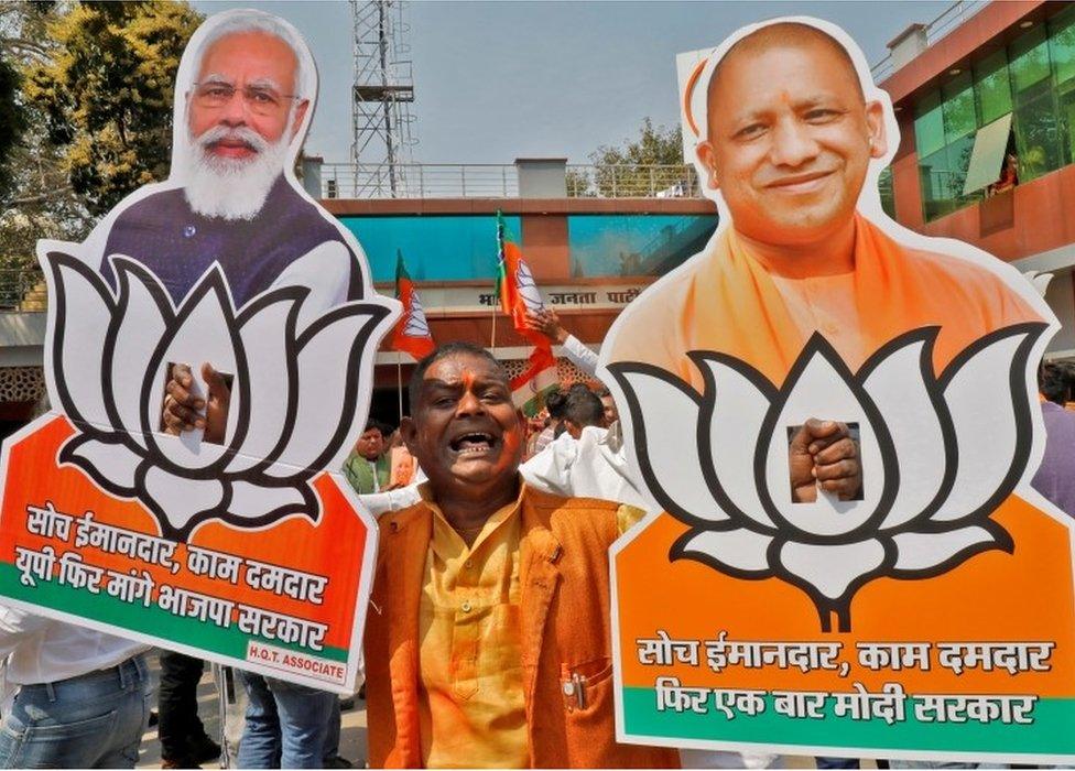 Supporter of India"s ruling party Bharatiya Janata Party (BJP) displays cut-outs of Prime Minister Narendra Modi and Chief Minister of Uttar Pradesh Yogi Adityanath as he celebrates after learning the initial poll results outside its party office in Lucknow, India, March 10, 2022