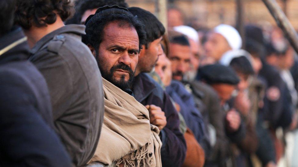 Afghan men stand in queues to receive food aid from a non-governmental organisation (NGO) in Kabul on December 25, 2022.