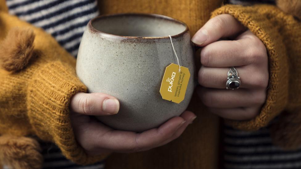 A woman holding a mug of Pukka Herbs tea