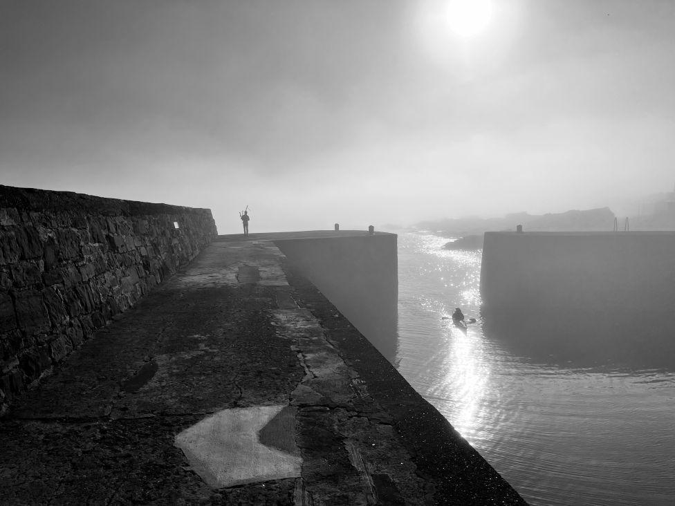 A lone piper playing in the distance while standing above a harbour
