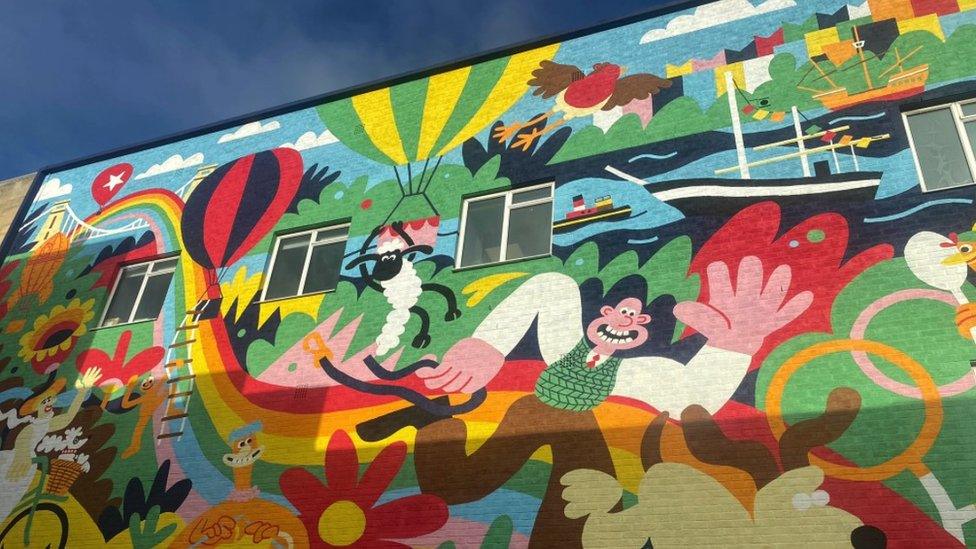 The mural in Bristol. The Clifton Suspension Bridge is painted in the top left hand corner of the mural, Bristol harbourside is painted in the top right hand corner and there are hot air balloons dotted around the mural.