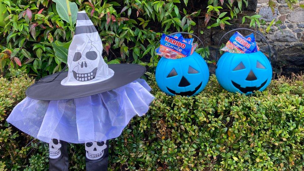 Blue Halloween buckets with sweets in on a hedge next to a Halloween decoration