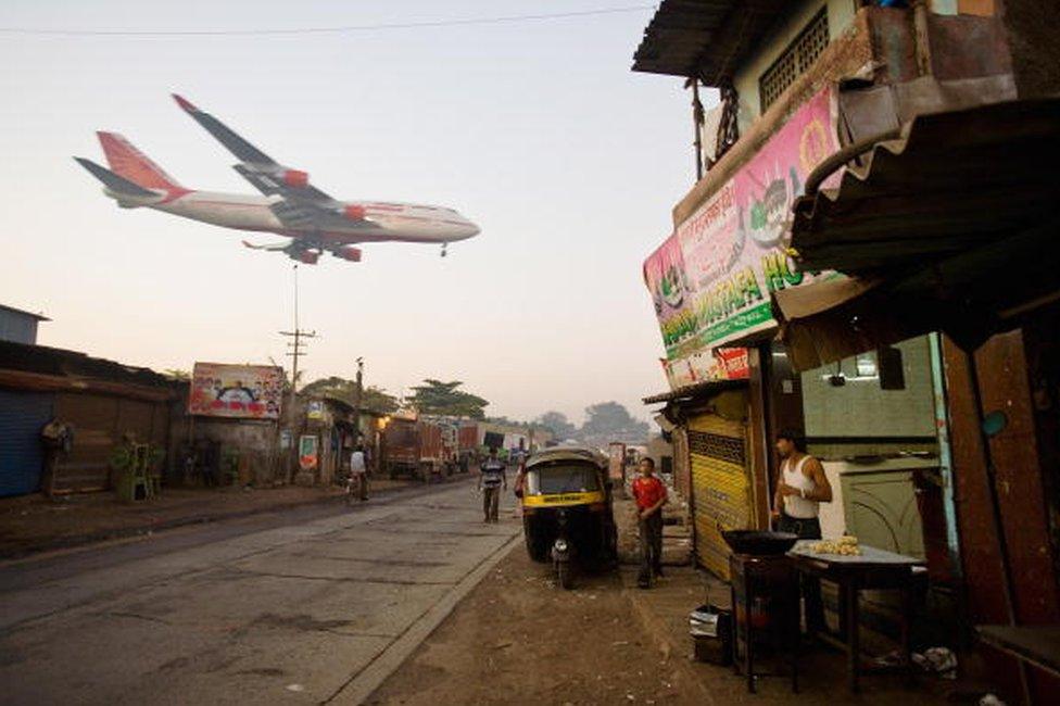 A man makes chapatis as an Air India passenger jet flies over the Jari Mari slum before landing at Mumbai Airport, on February 3, 2009 in Mumbai, India.