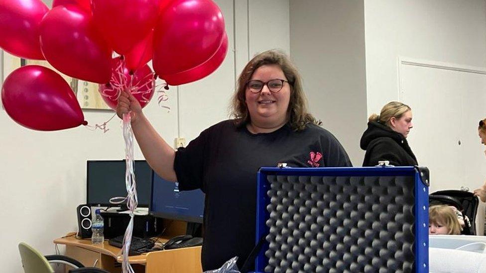 Olivia Cadwallader holding balloons and showing off the cuddle cot