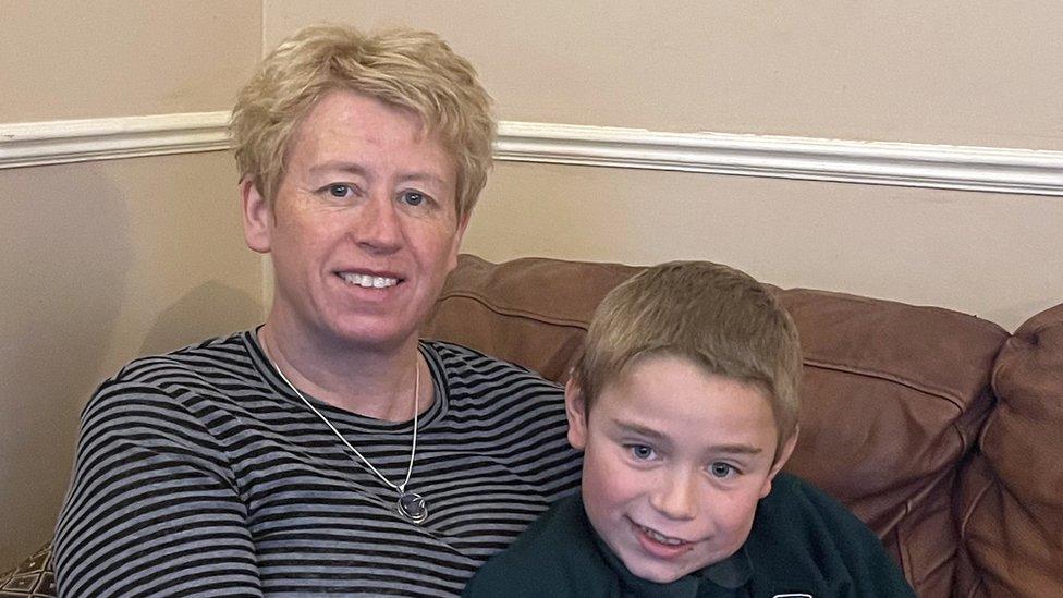 A white woman with short blonde hair sitting on a brown sofa with her young son