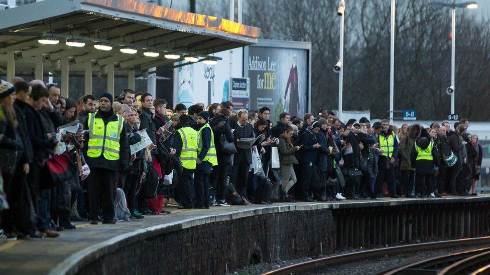 Commuters wait on a platform to catch a train toward central London at Clapham Junction station