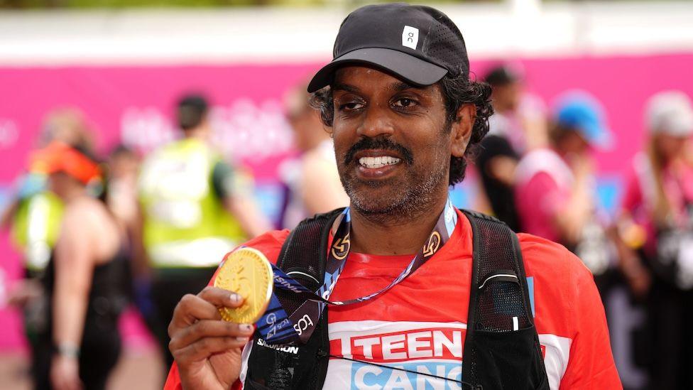 A picture of Romesh Ranganathan holding up his medal at the London Marathon finish line