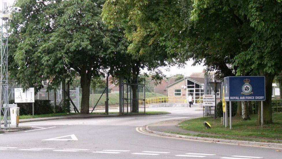 The entrance to RAF Digby, with trees and a road covering the building and a sign that says: "Royal Air Force Digby"