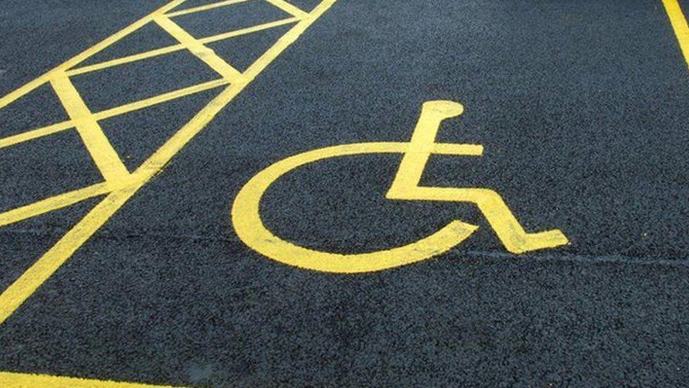 A disabled parking bay with yellow paint on the ground depicting a person in a wheelchair