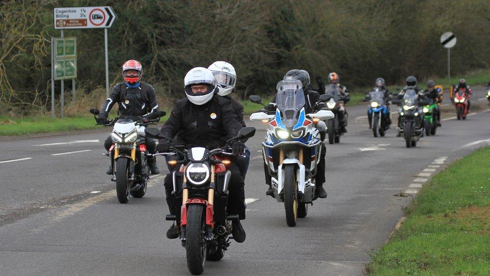 Line of motorbikes passing a sign to Cogenhoe