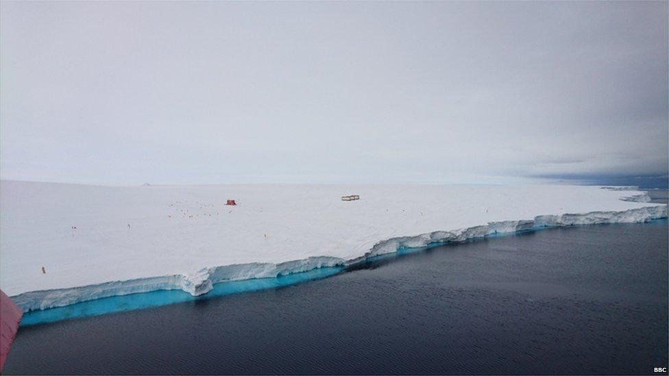 View of a large white mass of land, with a few tiny huts in the middle.