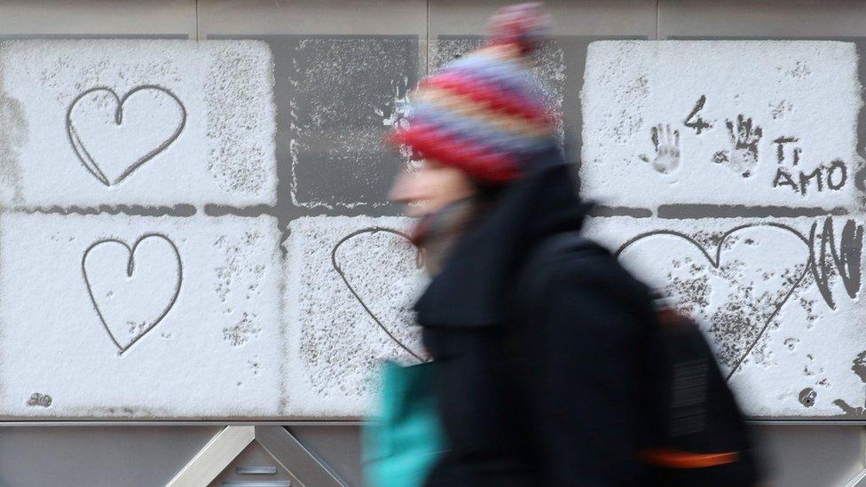 A woman walks past hearts drawn in the snow in Canary Wharf