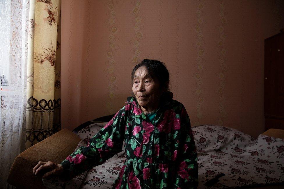 Autipana Audi (born.1941) sitting on her bed in her apartment. Yar-Sale village, Yamal Peninsula, Siberia, Russia.