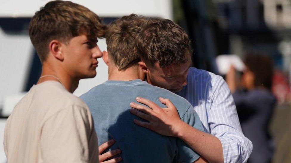 A group of men consoling each other outside a vigil in Nottingham.