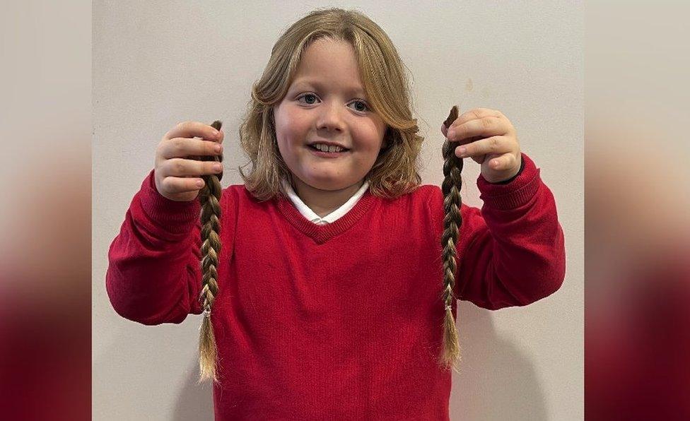 Noah smiling whilst holding two plaits of his hair up