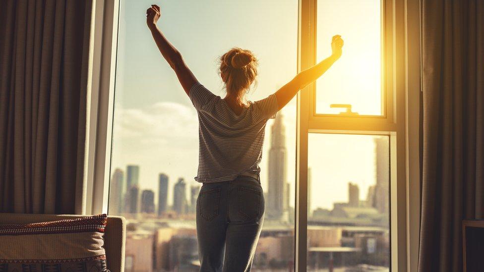 A woman stretches her arms in front of a window