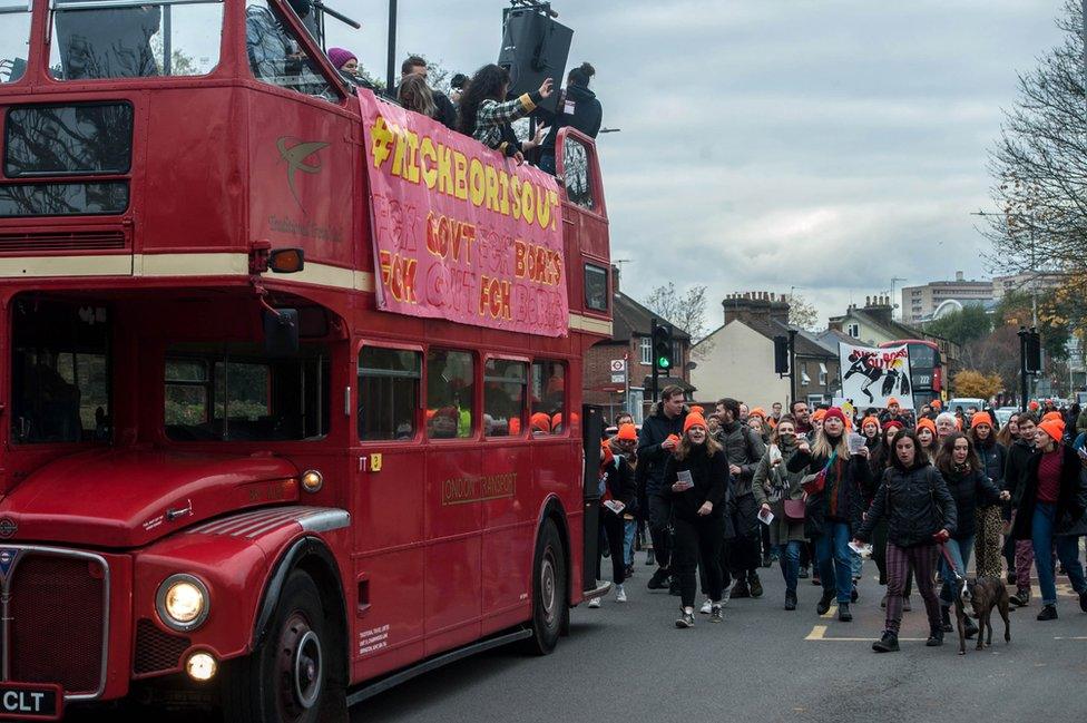 Anti-Boris Johnson protesters walk behind a red bus