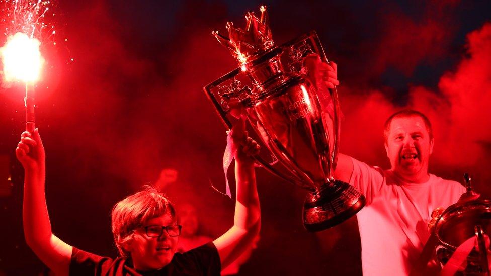 Two Liverpool fans celebrate with replica Premier League trophy outside Anfield