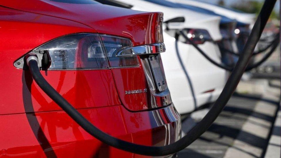 A bright red Tesla being charged at an EV charging station. Only the rear of the vehicle is visible.