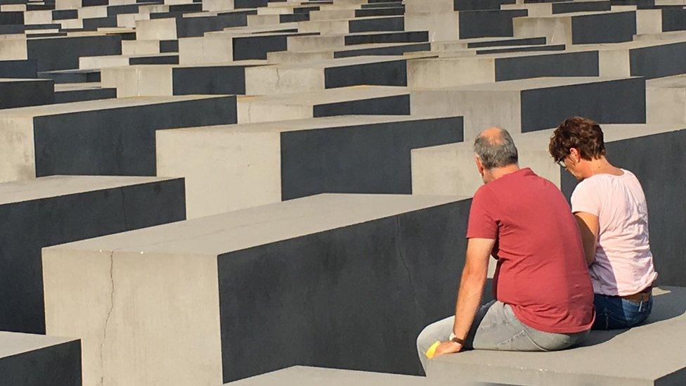 Two elderly people sit on a concrete slab at the Berlin Holocaust Memorial