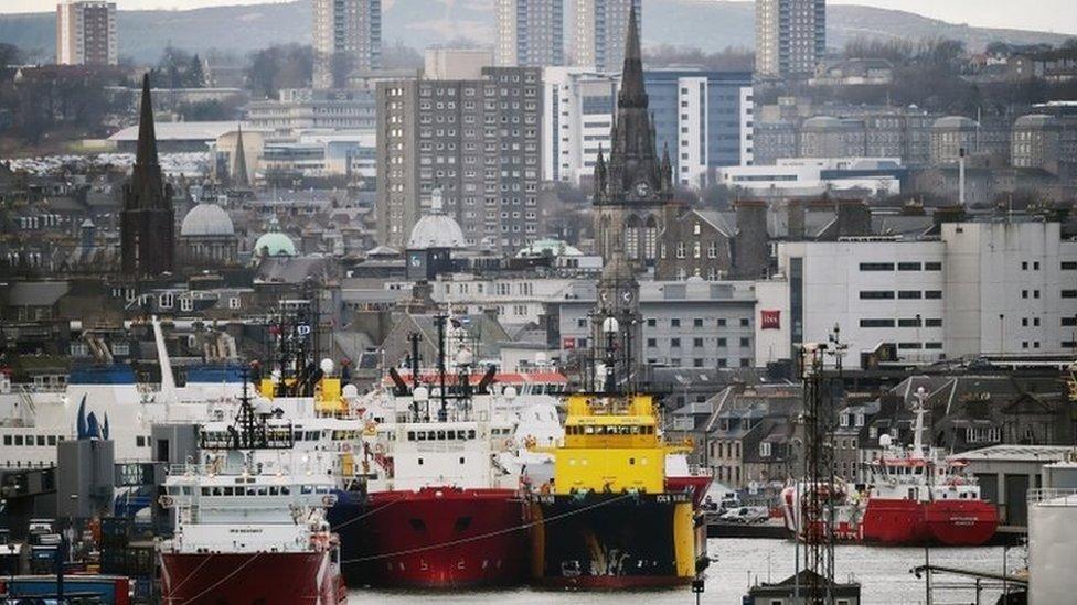 An image of Aberdeen harbour, with the granite buildings of the city in the background and ships moored in the harbour in the foreground