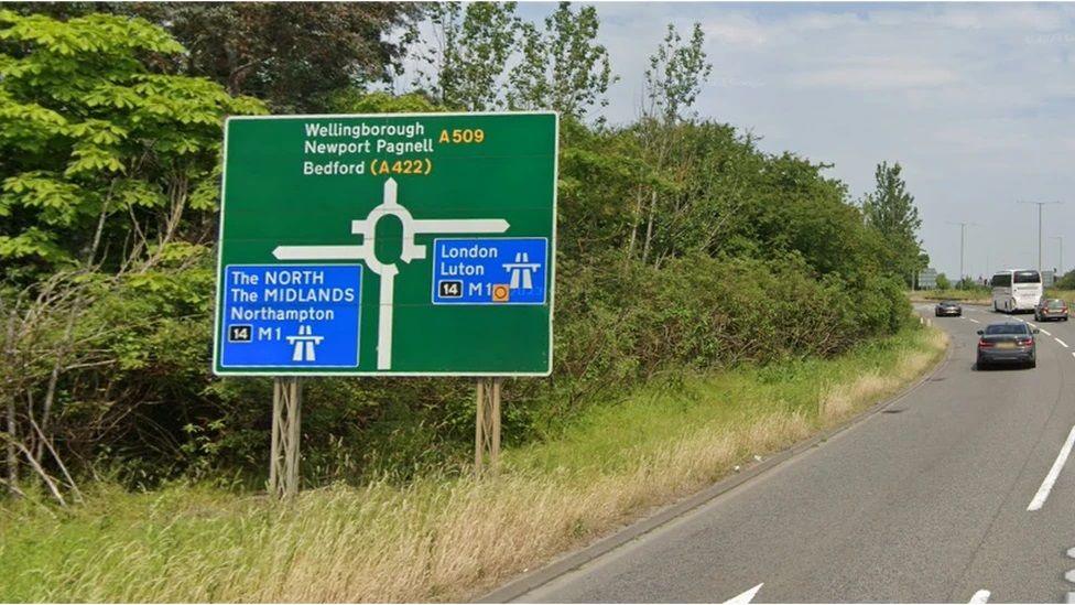 A green road sign showing a route towards the A509 on the side of a dual carriageway road.