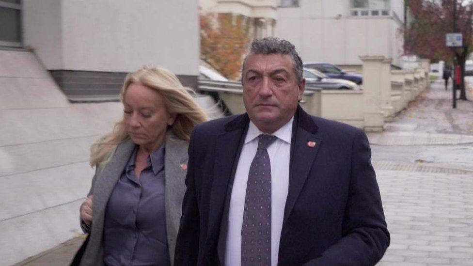 Man in suit with woman in grey jacket walk down street