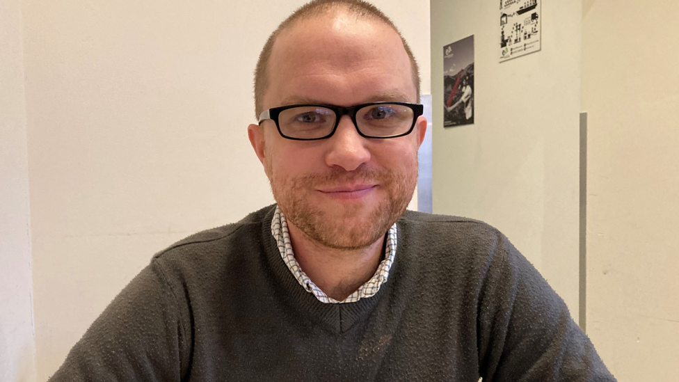 Roots development manager Daniel Smith sitting down looking at the camera wearing a grey jumper