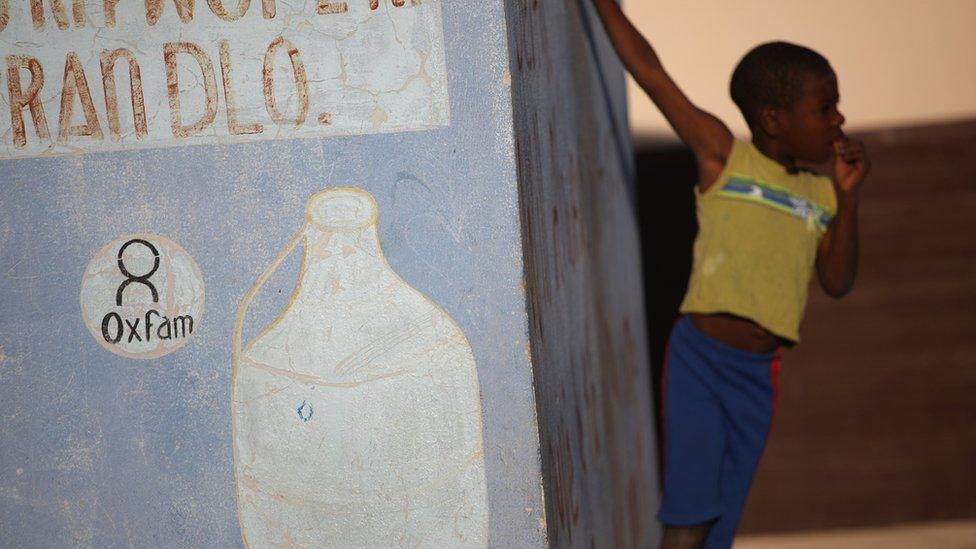 Boy stands next to Oxfam sign