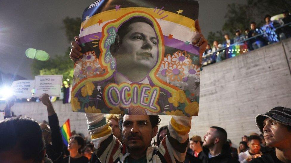 A person holds up a banner with Jesús Ociel Baena's face on it