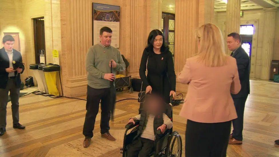 McMonagle is standing in the hall in Stormont. Michelle O'Neill is standing with her back to the camera. 