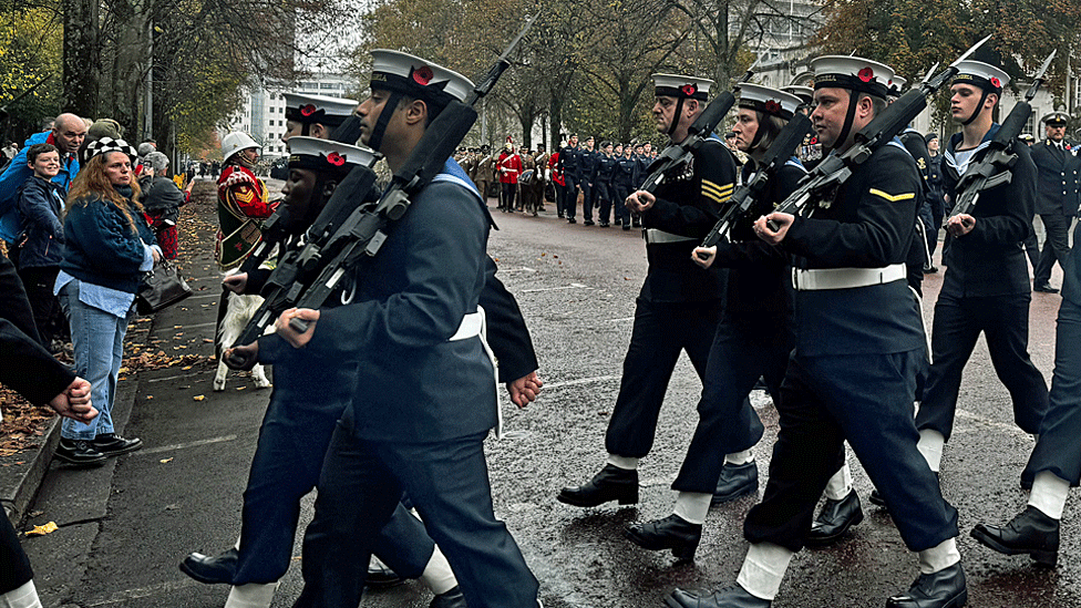 Procession of Armed Forces personnel as crowd of people line the route on a rainy Sunday morning