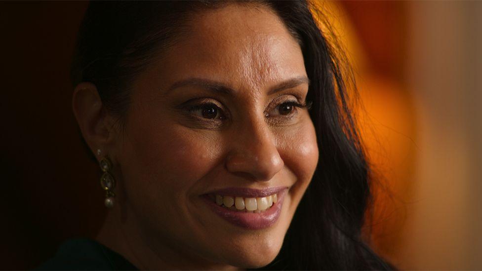 A still of Kirat from the Netflix documentary, in which it is a close up shot of her smiling. She is wearing earrings with a small pearl in her right ear.