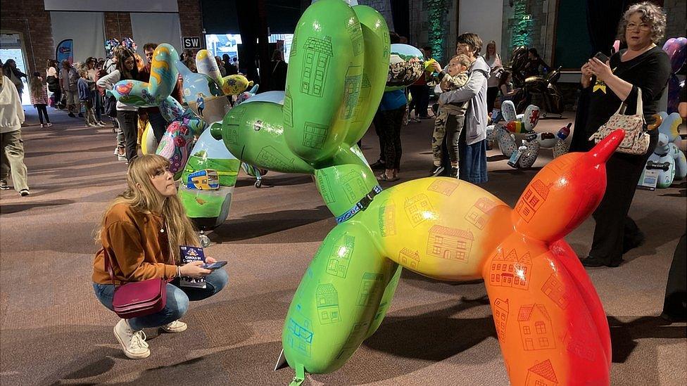 Woman crouching looking at colourful balloon dog sculpture