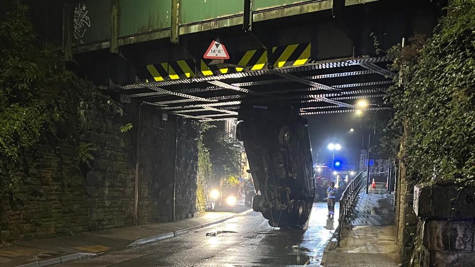 Van stuck vertically under railway bridge