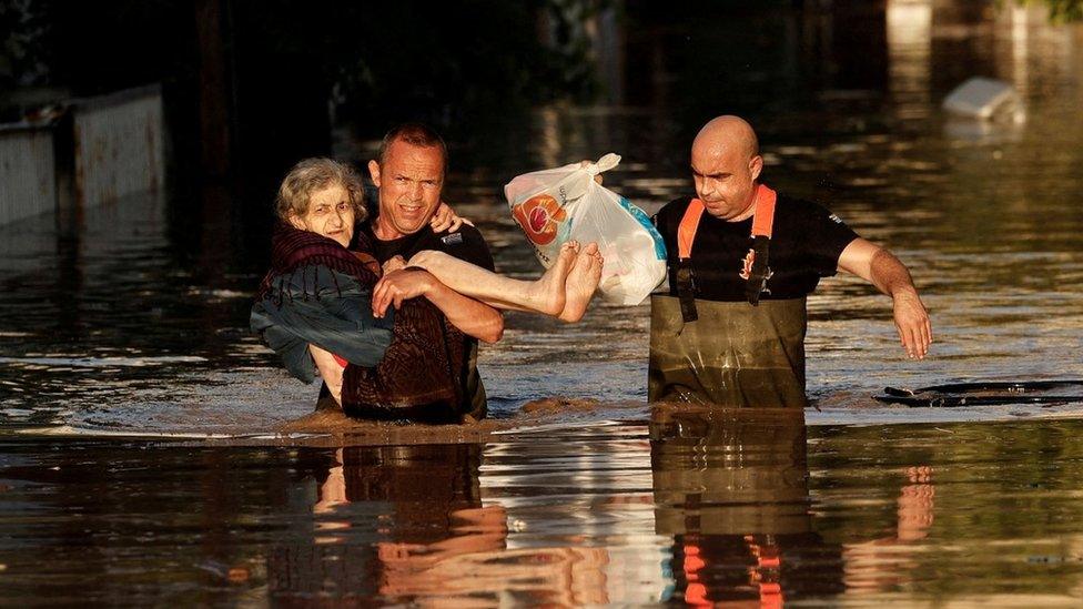 Greek firemen carry an elderly woman through floodwater