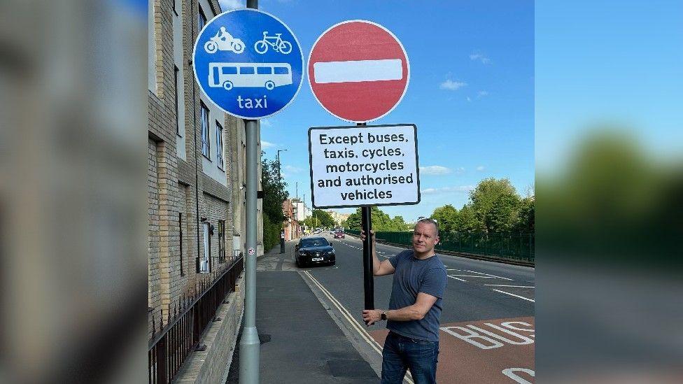  A man holds a home made "no entry" sign next to a blu