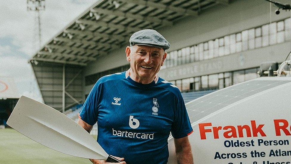 Frank Rothwell holding an oar at Oldham Athletic's stadium