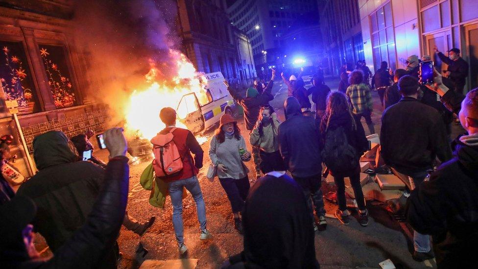 Protesters watch a police van burn